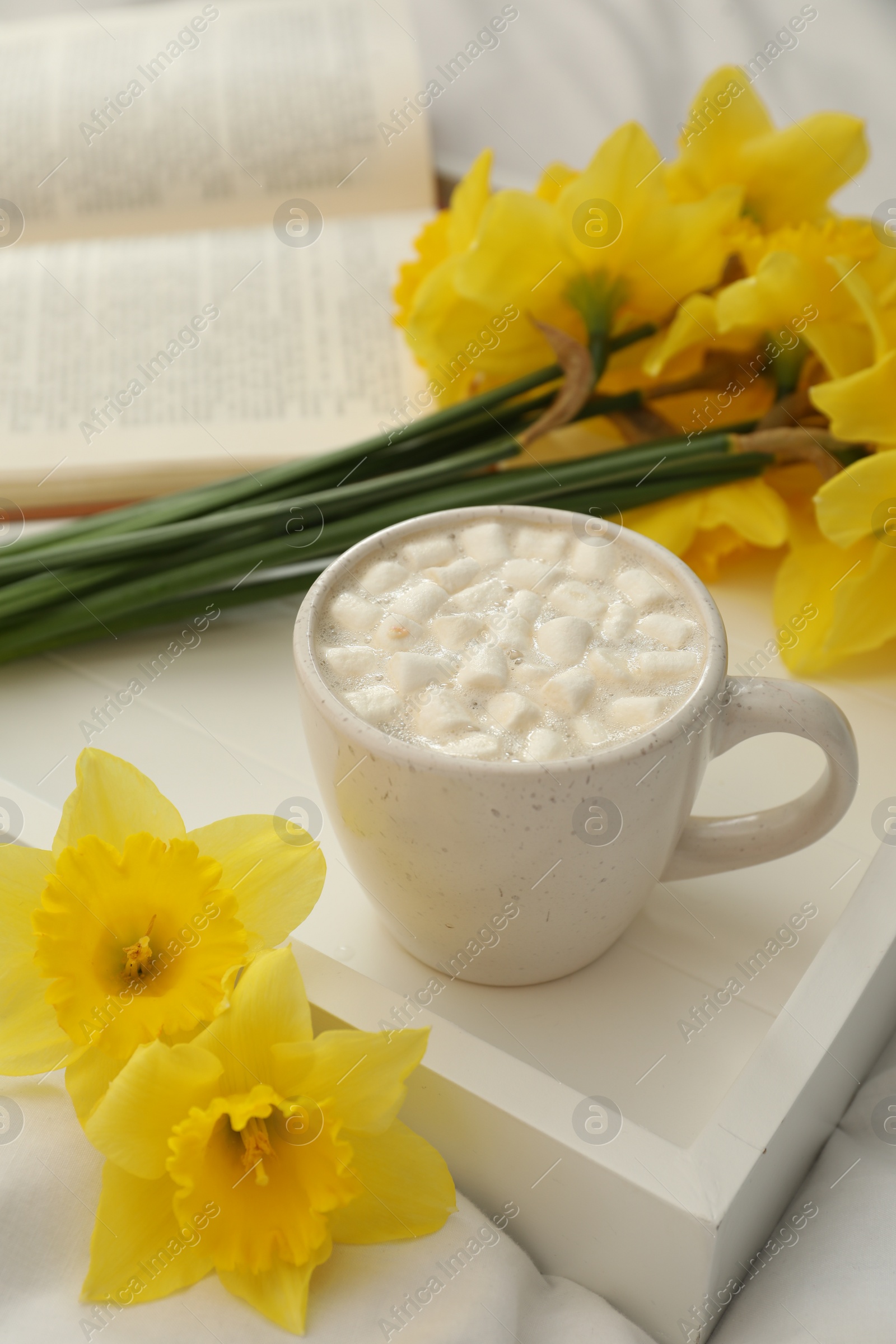 Photo of Beautiful daffodils and cup of hot drink on bed