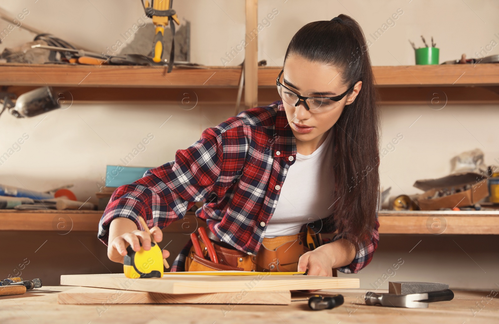 Photo of Female carpenter measuring wooden board in workshop