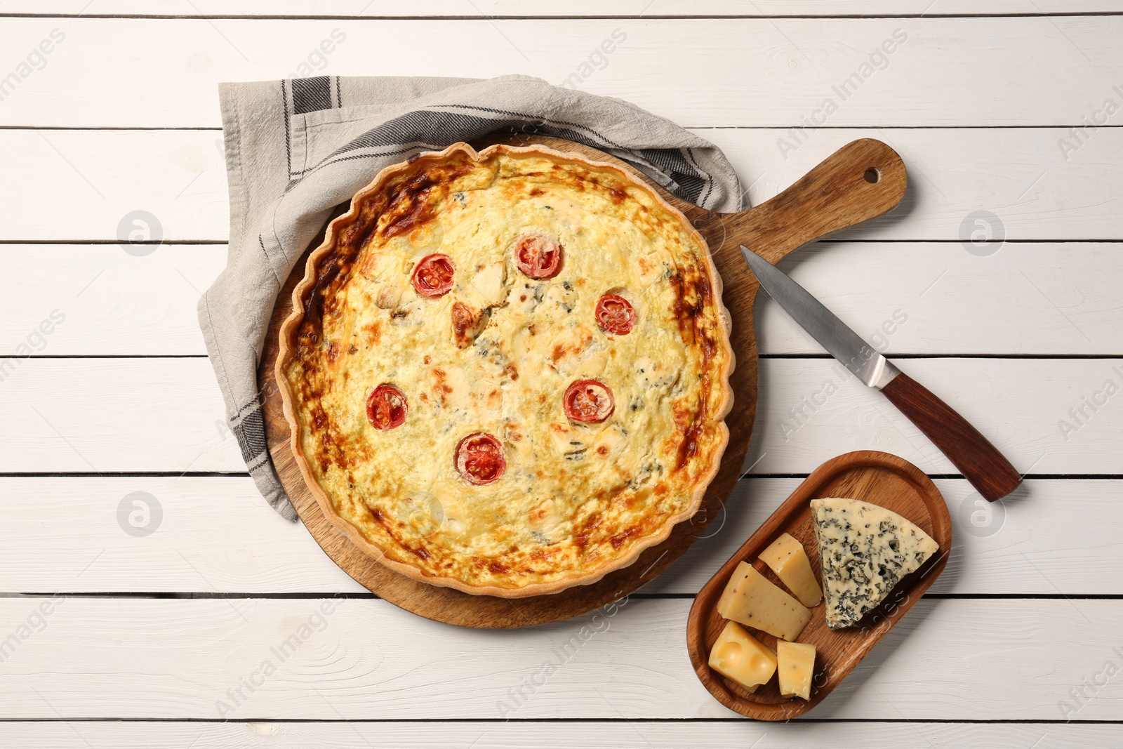 Photo of Delicious homemade cheese quiche, ingredients and knife on white wooden table, flat lay