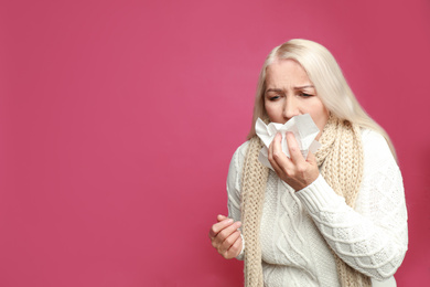 Mature woman sneezing on pink background, space for text. Cold symptoms