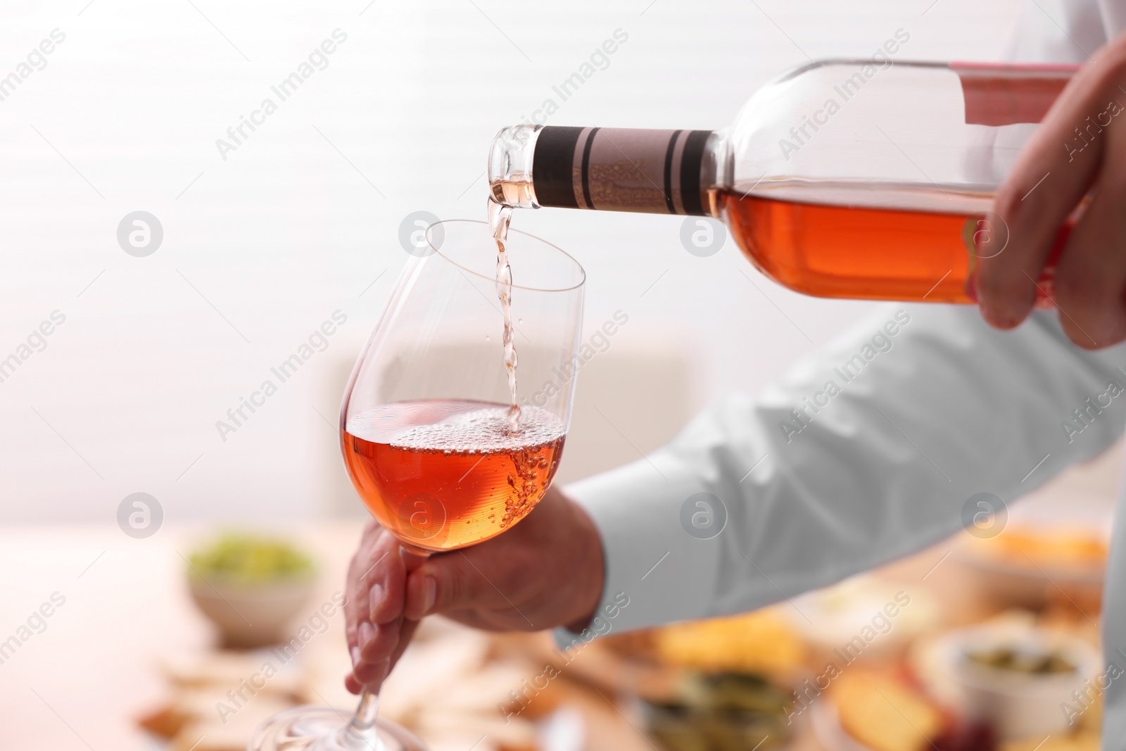 Photo of Man pouring rose wine from bottle into glass indoors, closeup