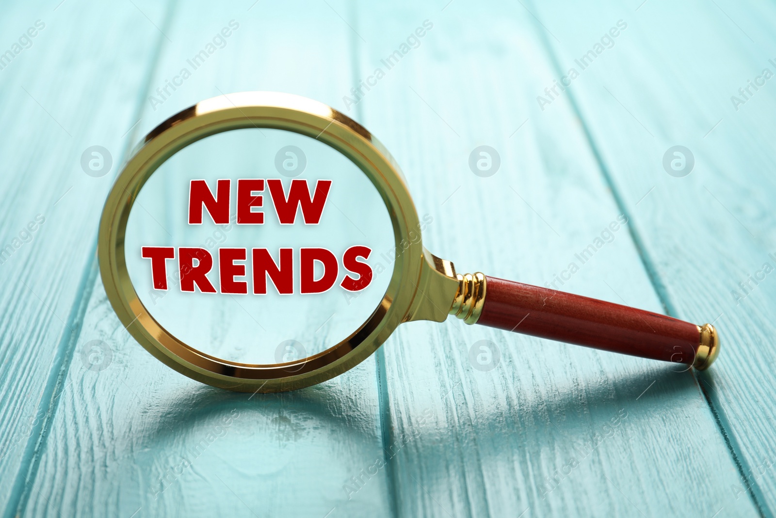 Image of Searching new and popular trends. Magnifying glass with words on turquoise wooden table, closeup
