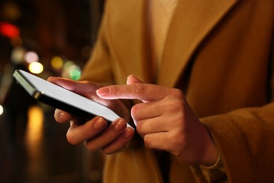 Photo of Woman using smartphone on night city street, closeup