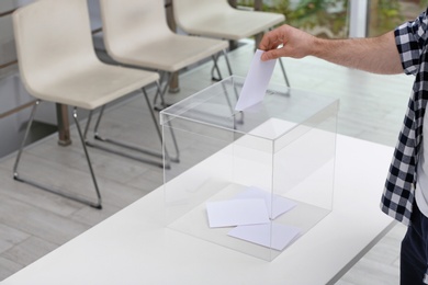 Photo of Man putting his vote into ballot box at polling station, closeup