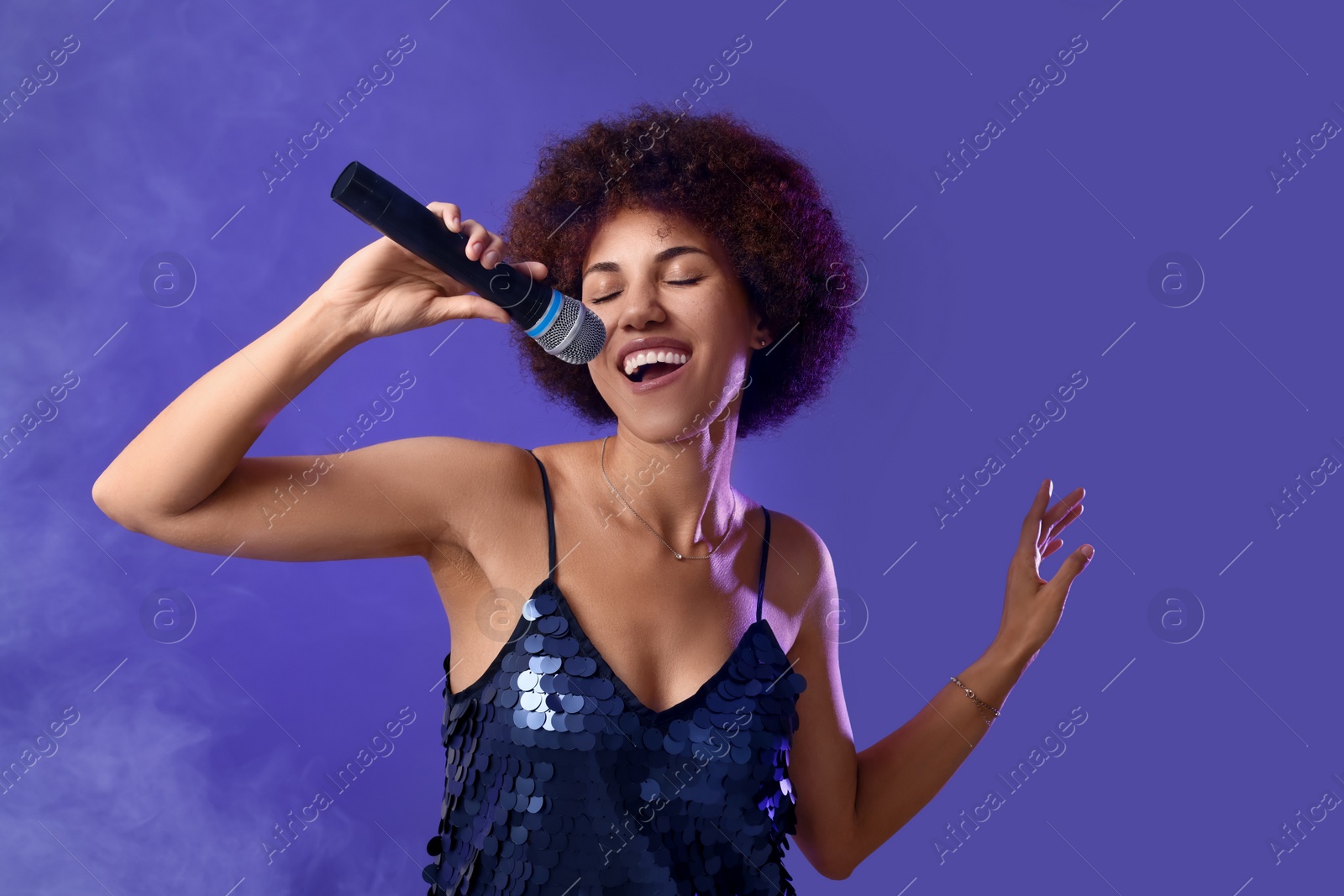 Photo of Curly young woman with microphone singing on purple background