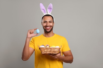 Photo of Happy African American man in bunny ears headband with Easter eggs on gray background