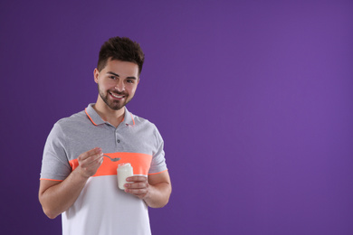 Photo of Happy young man with yogurt and spoon on purple background. Space for text