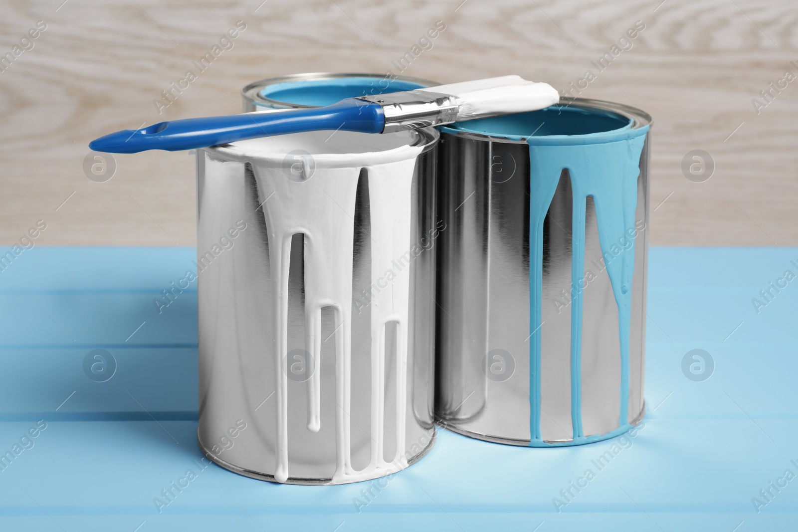 Photo of Cans of paints and brush on light blue wooden table