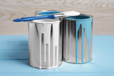 Photo of Cans of paints and brush on light blue wooden table