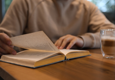 Photo of Man with coffee reading book at wooden table, closeup