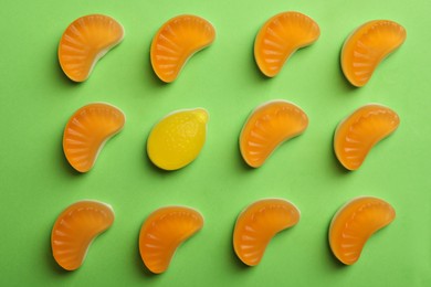 Delicious gummy orange and lemon candies on green background, flat lay