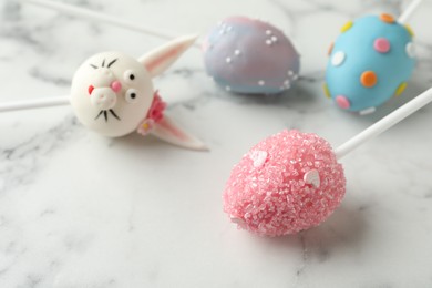 Delicious sweet cake pops for Easter celebration on white marble table, closeup