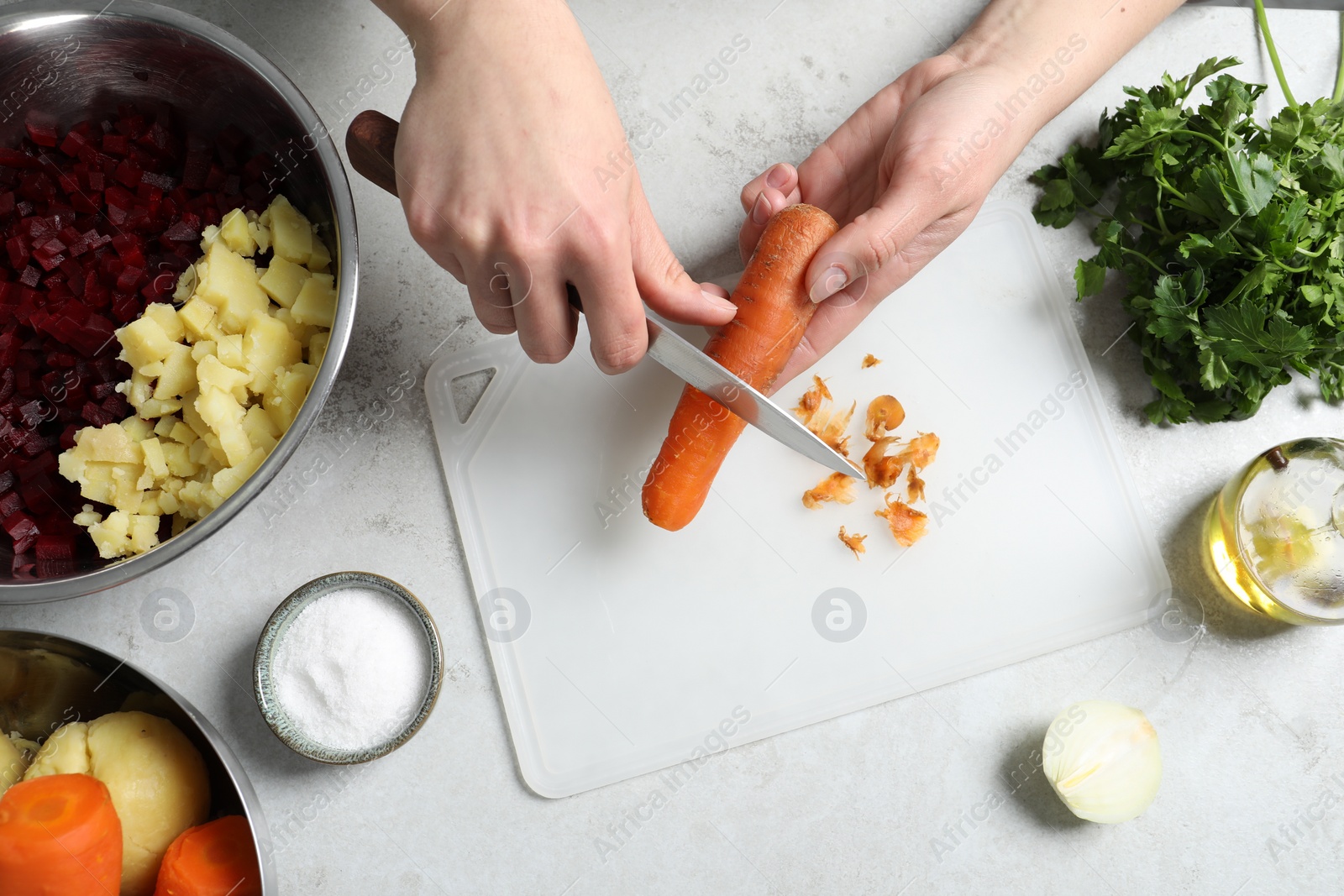 Photo of Woman peeling boiled carrot at white table, top view. Cooking vinaigrette salad