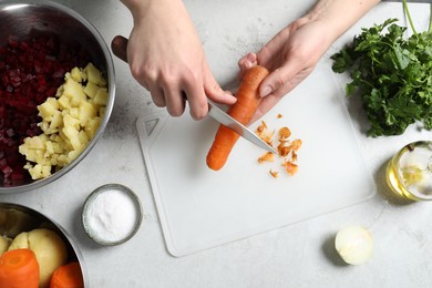 Photo of Woman peeling boiled carrot at white table, top view. Cooking vinaigrette salad