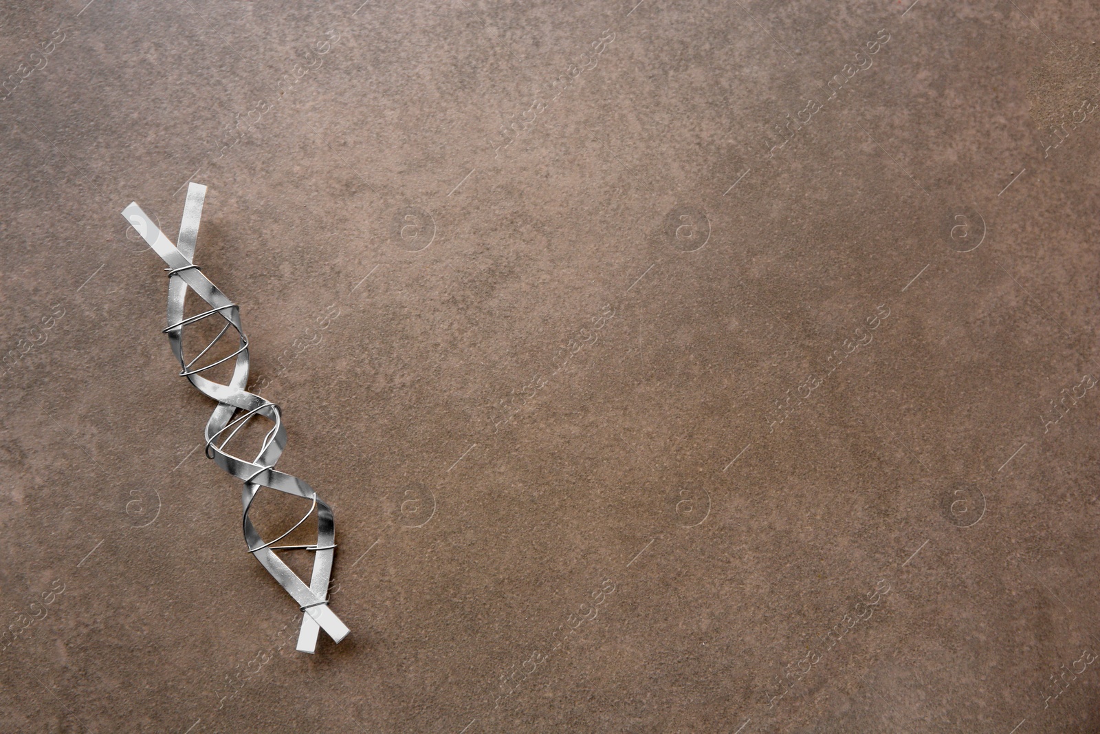 Photo of DNA molecule model made of metal on brown background, top view. Space for text