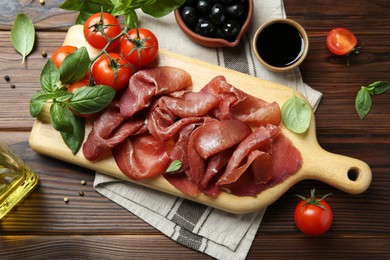 Photo of Board with delicious bresaola and other snacks served on wooden table, flat lay