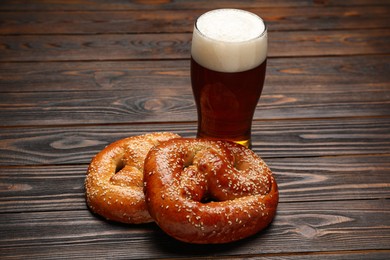 Photo of Tasty freshly baked pretzels and glass of beer on wooden table