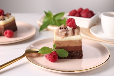 Photo of Piece of triple chocolate mousse cake with raspberries served on white table, closeup