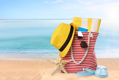 Image of Stylish bag with different accessories on sandy beach, space for text 