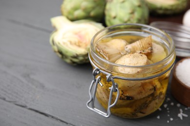 Photo of Jar of delicious artichokes pickled in olive oil on grey wooden table, closeup. Space for text