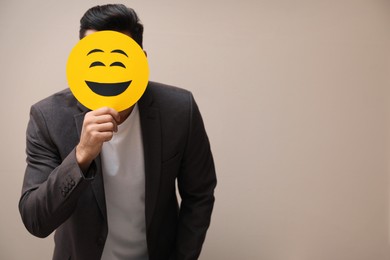 Photo of Man hiding emotions using card with drawn smiling face on beige background. Space for text