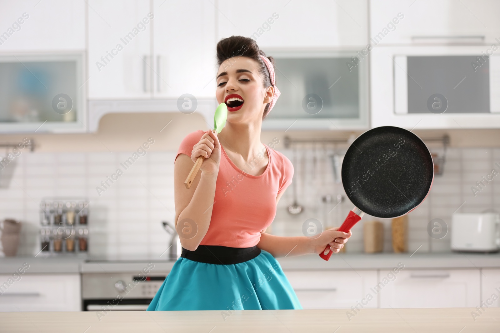 Photo of Funny young housewife using spoon as microphone in kitchen