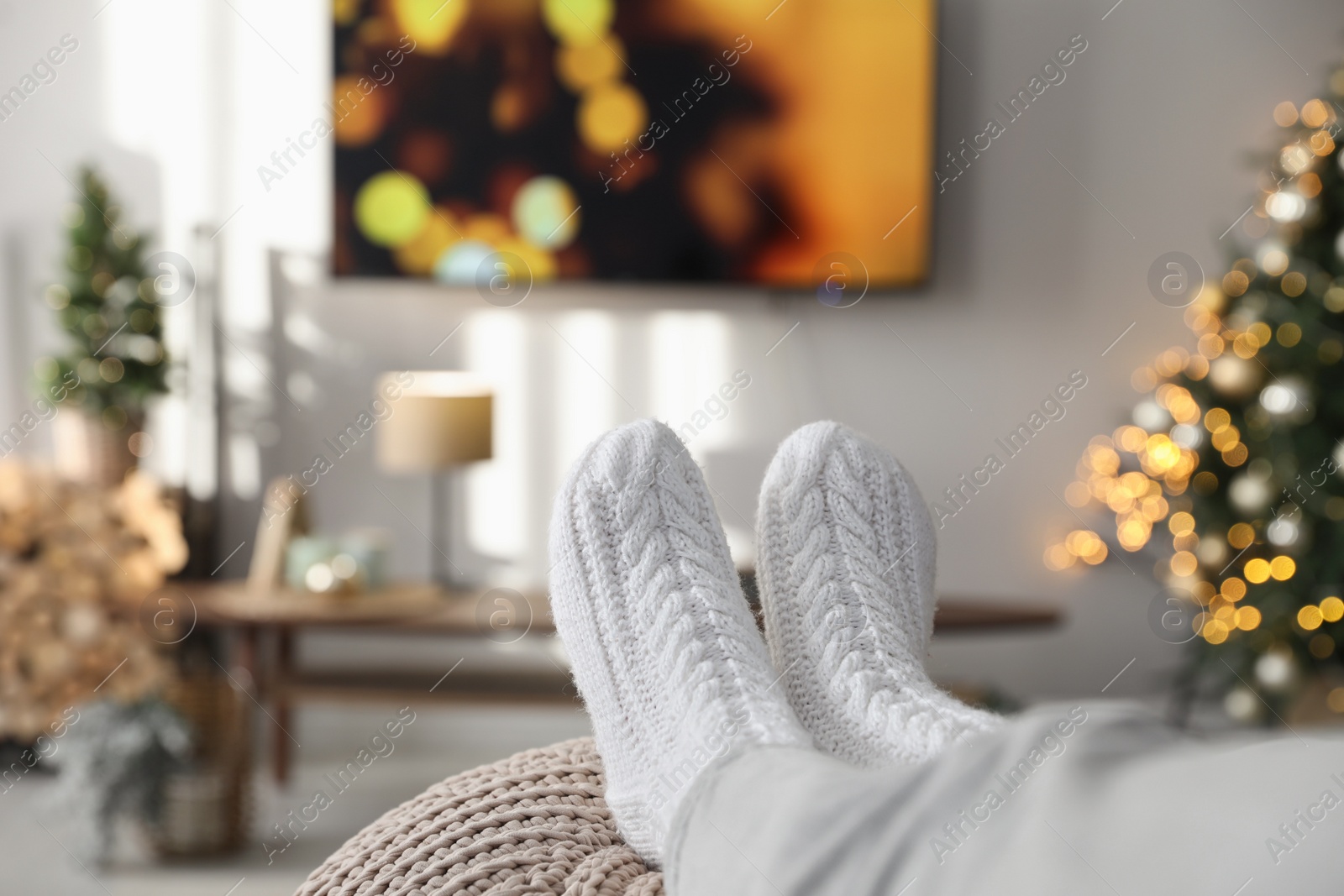 Photo of Woman wearing knitted socks in room decorated for Christmas, closeup