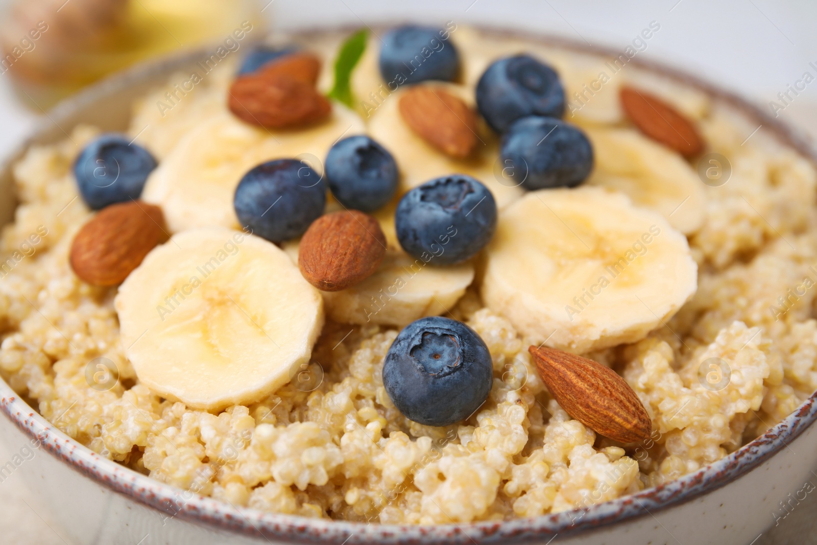 Photo of Bowl of delicious cooked quinoa with almonds, bananas and blueberries, closeup