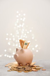 Photo of Piggy bank with euro banknote and coins on grey table against blurred lights, space for text