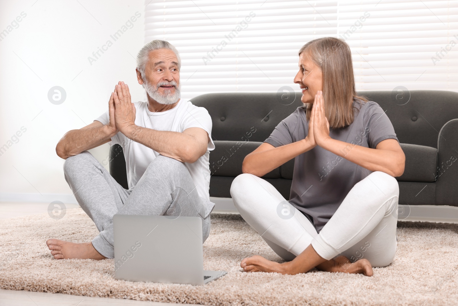 Photo of Senior couple practicing yoga with laptop at home