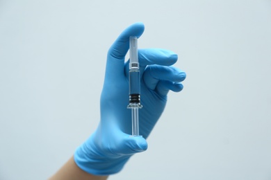 Doctor holding syringe with COVID-19 vaccine on light background, closeup