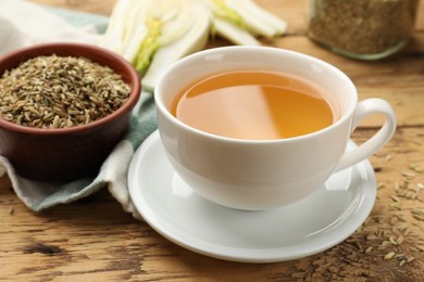 Fennel tea in cup and seeds on wooden table, closeup
