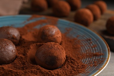 Photo of Delicious chocolate truffles with cocoa powder on blue plate, closeup