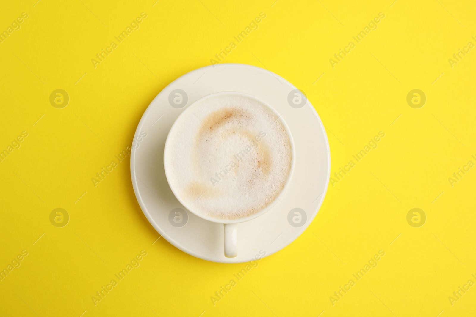 Photo of Tasty cappuccino in coffee cup on yellow background, top view