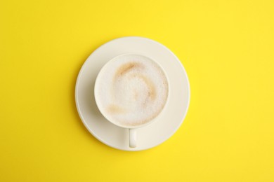 Photo of Tasty cappuccino in coffee cup on yellow background, top view