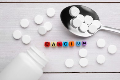 Photo of Word Calcium made of colorful plastic beads with letters, medical bottle and pills on white wooden table, flat lay