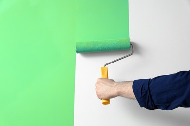 Photo of Man applying light blue paint with roller brush on white wall, closeup