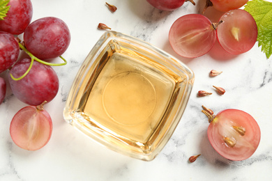 Photo of Bowl of natural grape seed oil on white marble table, flat lay. Organic cosmetic