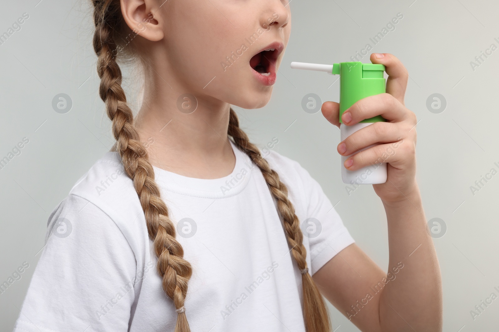 Photo of Little girl using throat spray on light grey background, closeup