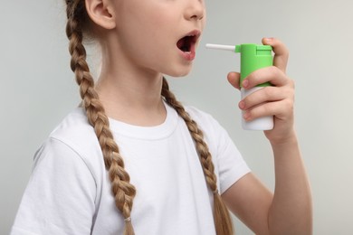 Little girl using throat spray on light grey background, closeup