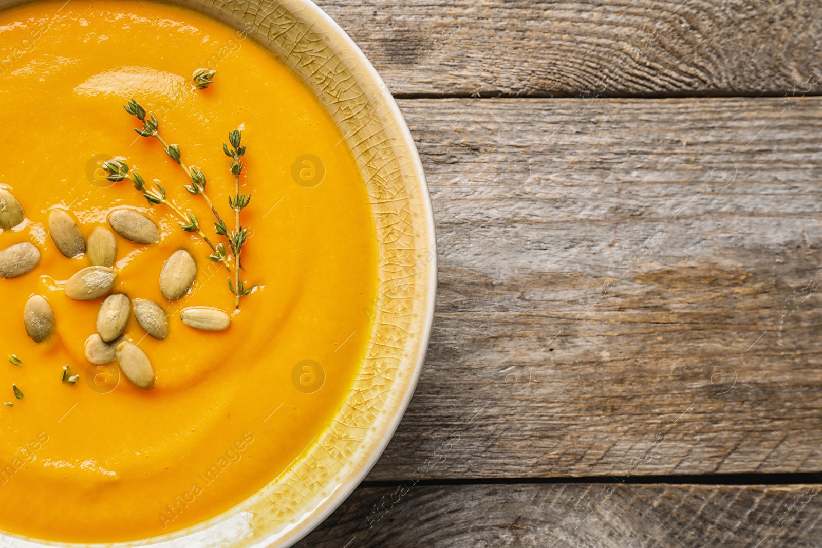 Photo of Bowl with tasty pumpkin soup and space for text on wooden table, top view