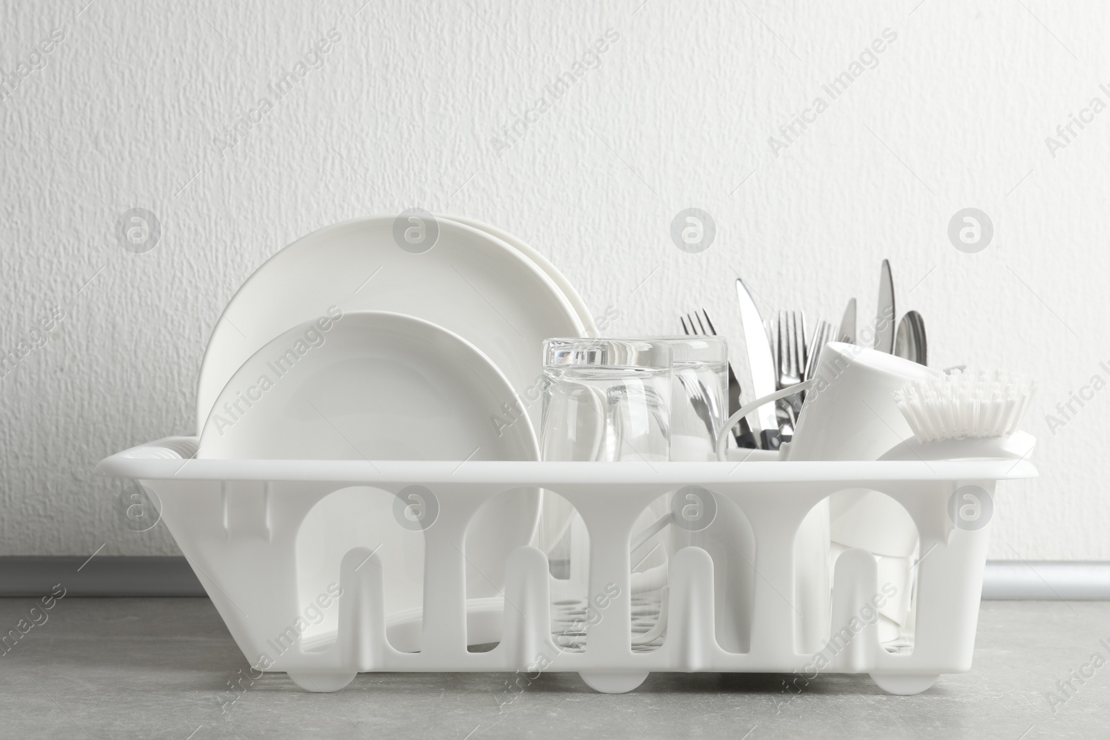 Photo of Drying rack with clean dishes and cutlery on table near light wall