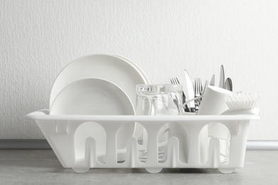 Drying rack with clean dishes and cutlery on table near light wall