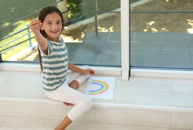 Little girl drawing rainbow near window indoors. Stay at home concept