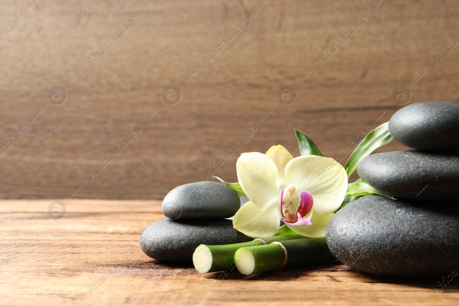 Photo of Spa stones, bamboo stems and beautiful orchid flower on wooden table, space for text