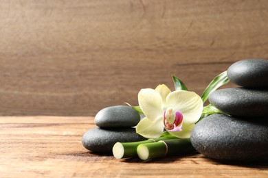 Spa stones, bamboo stems and beautiful orchid flower on wooden table, space for text