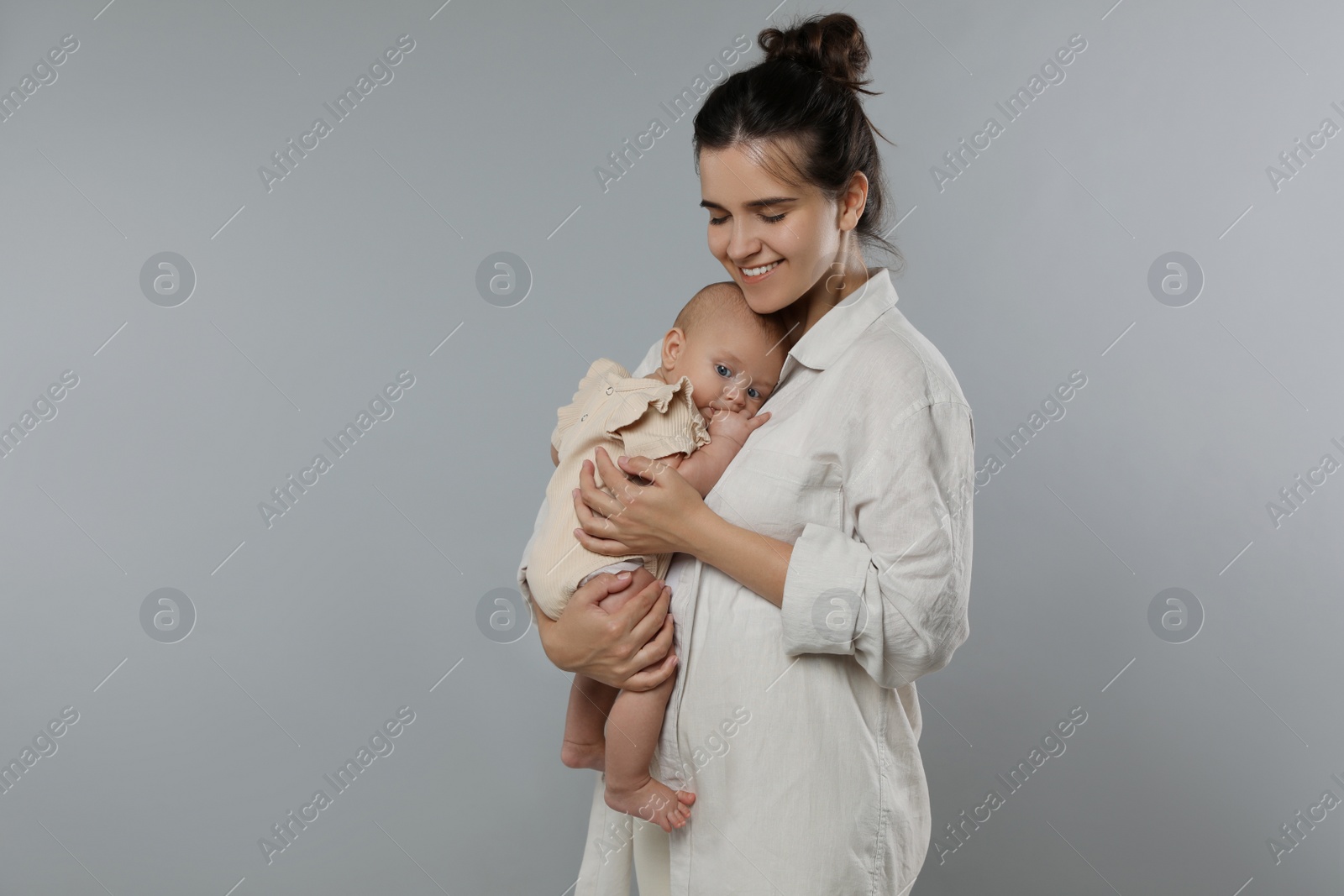 Photo of Beautiful mother with her cute baby on grey background. Space for text