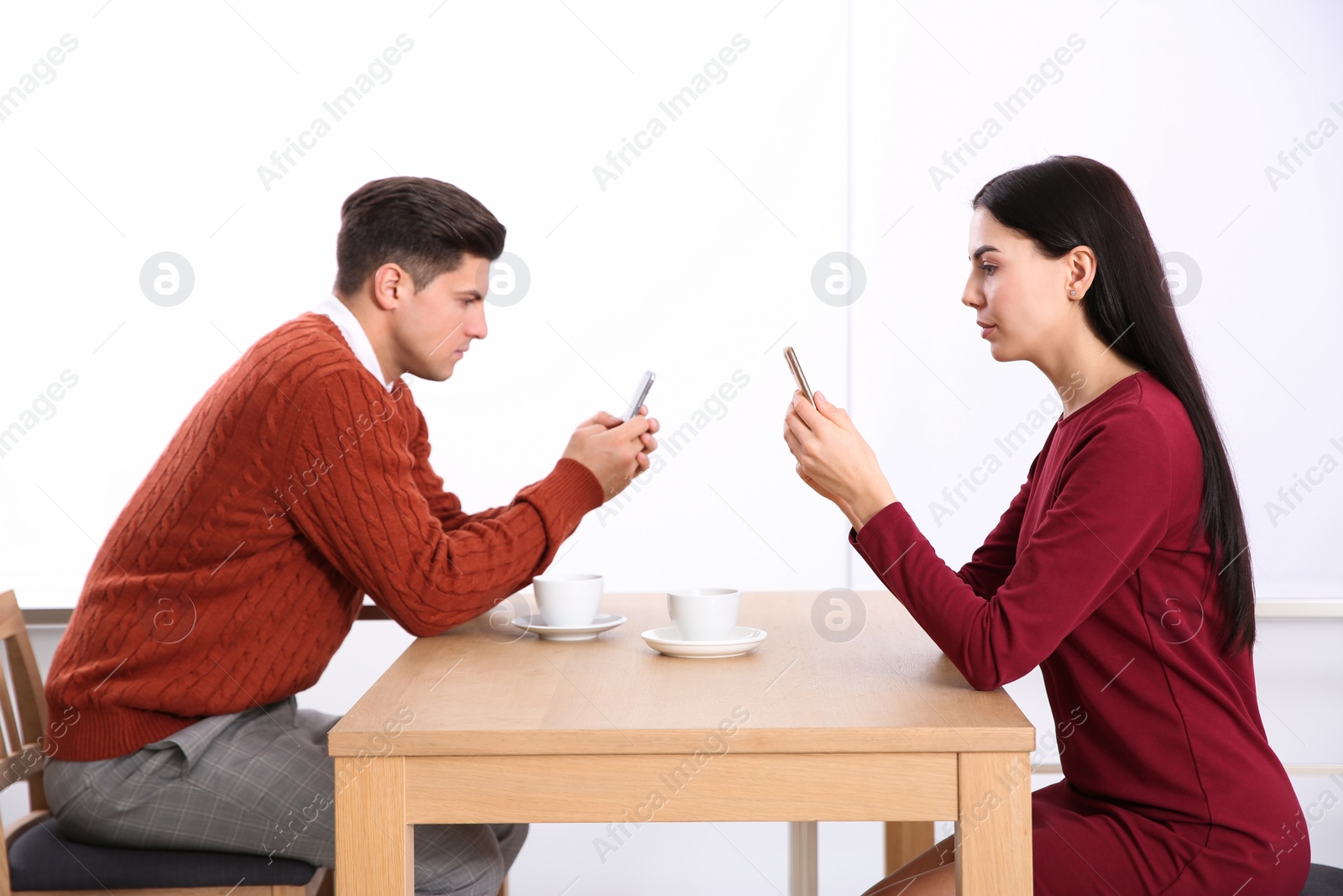 Photo of Couple addicted to smartphones ignoring each other in cafe. Relationship problems