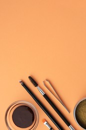 Flat lay composition with eyebrow henna and professional tools on orange background, space for text
