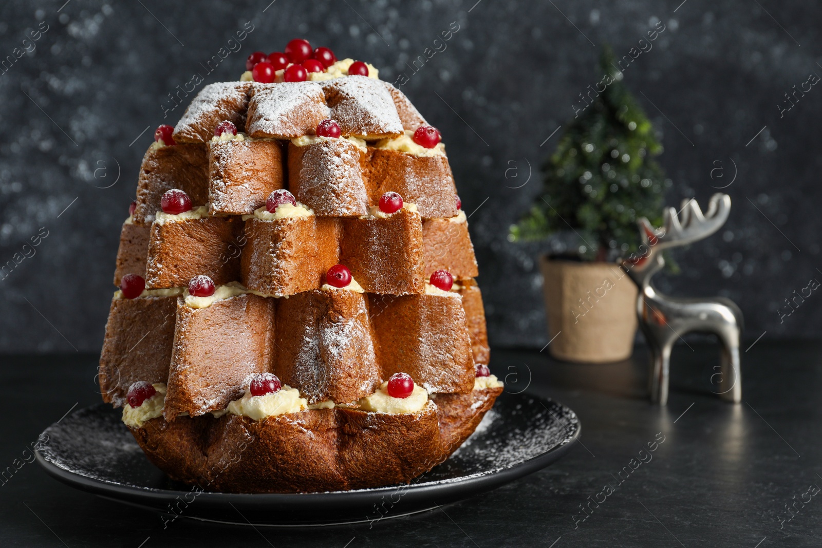 Photo of Delicious Pandoro Christmas tree cake with powdered sugar and berries near festive decor on black table